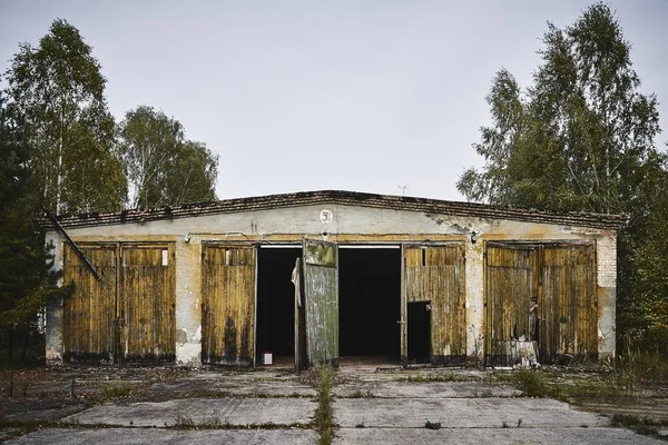 Starý opuštěný sklad s rozbitými dveřmi obklopenými stromy — Stock fotografie