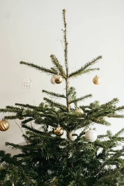 在白色的墙壁上装饰着金黄色灌木的一棵圣诞树的垂直照片 — 图库照片