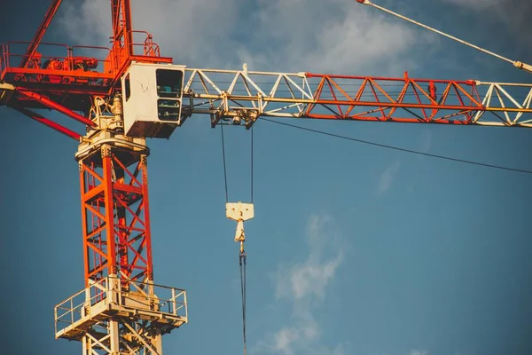 A white and red construction crane under a blue cloudy sky and sunlight