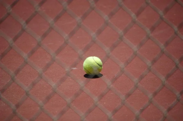 Tennisboll Röd Bana Solljus Bakom Ett Suddigt Trådburet Staket — Stockfoto