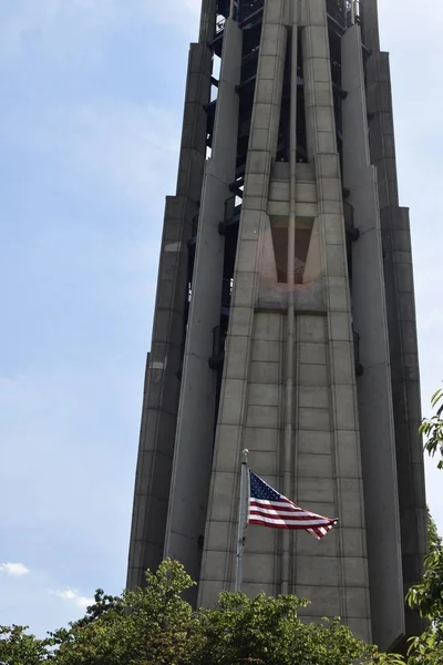 Wysoka Wieża Otoczona Zielenią Amerykańską Flagą Przed Nią Pod Słońcem — Zdjęcie stockowe