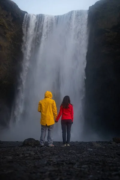Coppia indossa abiti rossi e gialli in piedi su una scogliera con una cascata contro di esso — Foto Stock