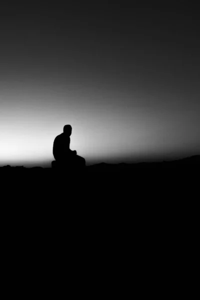 Silhouette of a person sitting on a wood surrounded by hills under sunlight — Stock Photo, Image