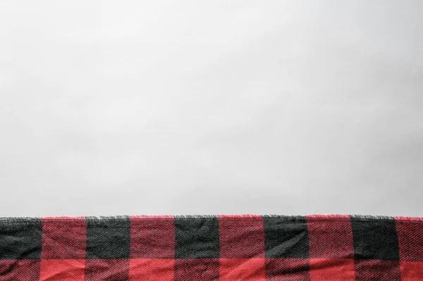 A red and black flannel texture on a white surface with empty space for text