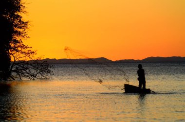 A silhouette of a person on a boat fishing in the sea during sunset in Ometepe, Nicaragua clipart