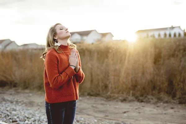 White female standing in the field praying with closed eyes during sunrise — 스톡 사진