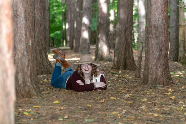一个女人 头戴一顶帽子 身穿红衫 躺在被树木和树叶环绕的森林里的地上 — 图库照片