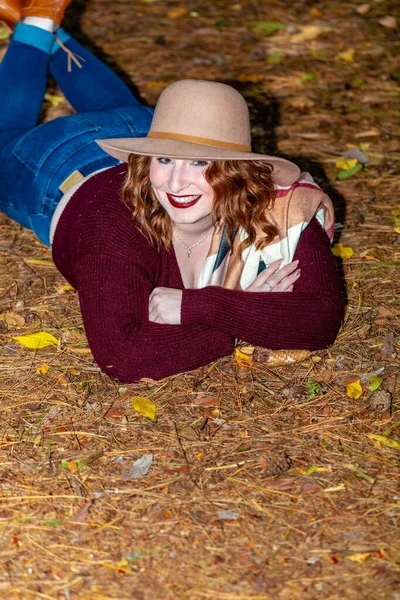 一个女人 头戴一顶帽子 身穿红衫 躺在被树木和树叶环绕的森林里的地上 — 图库照片