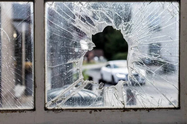 A broken glass window surrounded by rusty old frames with cars and a park on the background