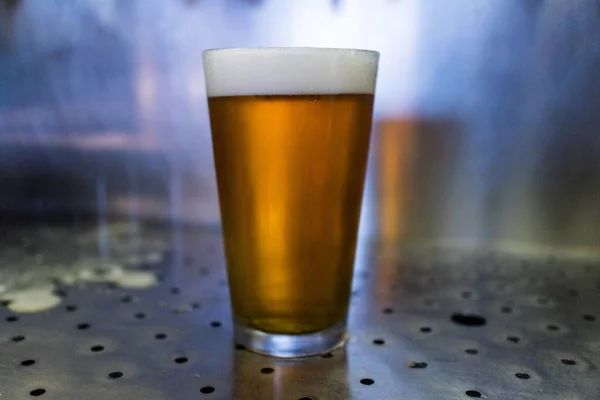 A closeup of a glass of beer on a metallic table with a blurry background