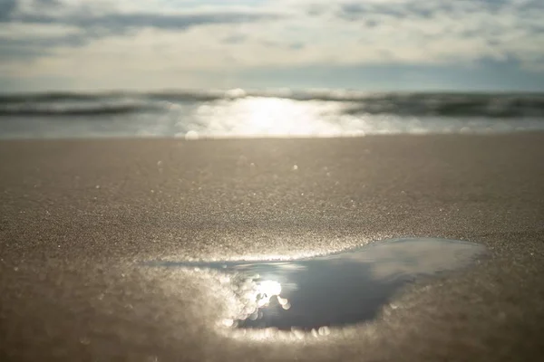 Gros plan d'une plage couverte de gouttes d'eau sous la lumière du soleil avec la mer sur le fond flou — Photo