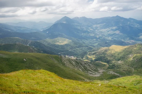 Hügellandschaft im Grünen mit felsigen Bergen unter wolkenverhangenem Himmel im Hintergrund — Stockfoto