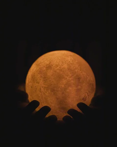 Closeup of hands holding a red moon figure with lights against a dark background — Stok Foto