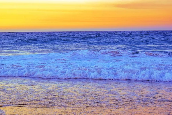 Paesaggio di una spiaggia circondata da onde marine durante un tramonto arancione la sera — Foto Stock