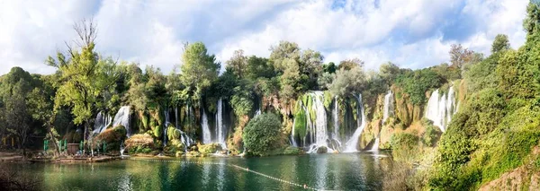 Mesmerizing panoramic shot of waterfalls flowing into the river in the middle of the park