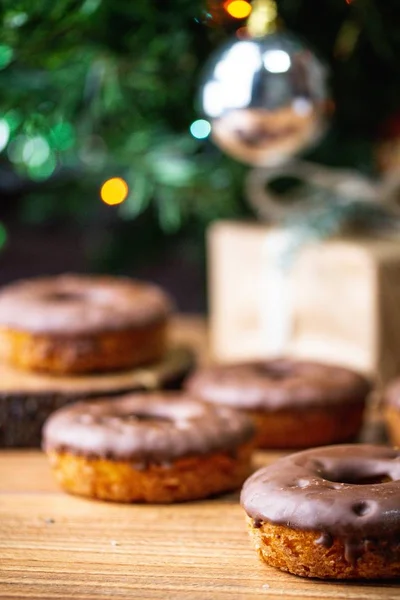 Vertical selective focus shot of doughnut in front of blurry decorated Christmas tree and doughnuts — 스톡 사진