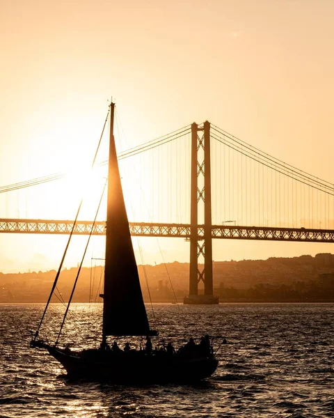 Verticale lage hoek opname van de 25 April brug tijdens zonsondergang met silhouetted boot op de voorgrond — Stockfoto