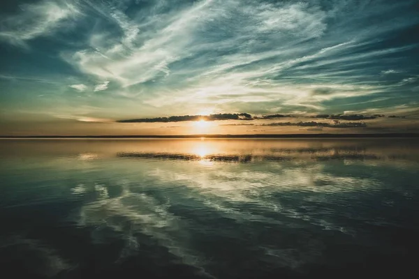 Pôr do sol e as nuvens do céu refletidas no oceano abaixo — Fotografia de Stock