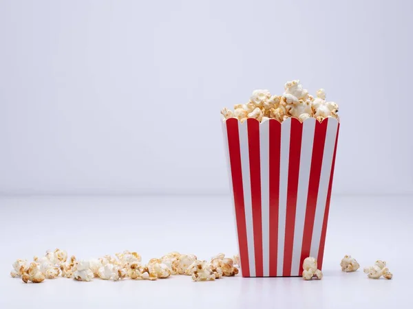 Pappbecher Popcorn und etwas Popcorn verstreut auf einer weißen Fläche — Stockfoto