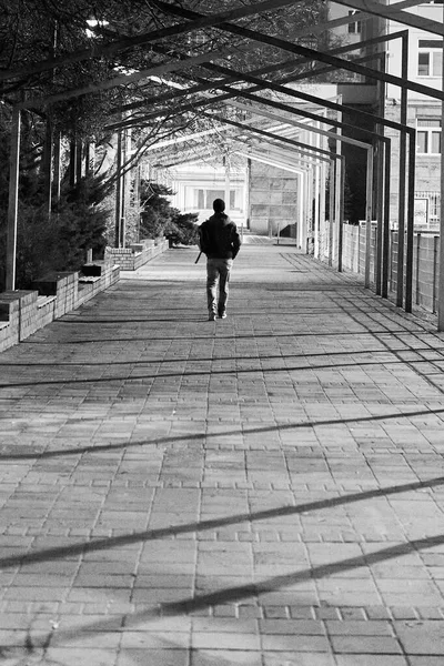 Вертикальный серый снимок мужчины, идущего по тротуару — стоковое фото