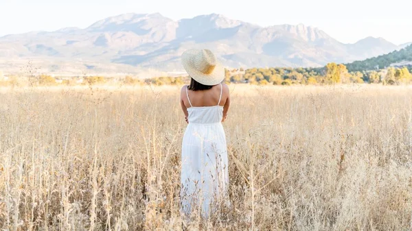 Széles kép egy fehér ruhás nőről, háttal a kamerának, ahogy a búzamezőn áll. — Stock Fotó