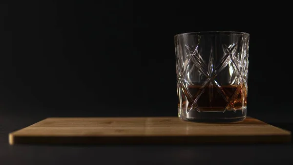Verre de whisky sur une planche à découper sur un fond noir flou — Photo