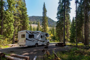 Beautiful campsite in the mountains with an RV and wooden bench.