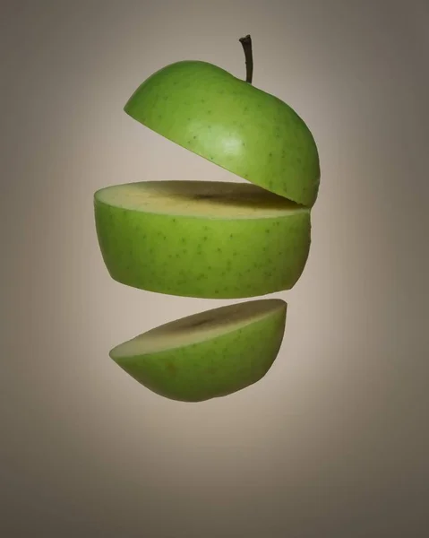 Tiro vertical de uma maçã suculenta verde cortada em três pedaços — Fotografia de Stock