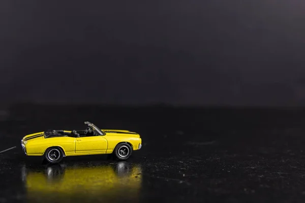 Foto selectivo de enfoque de un coche de juguete amarillo con rayas negras en una superficie negra. — Foto de Stock