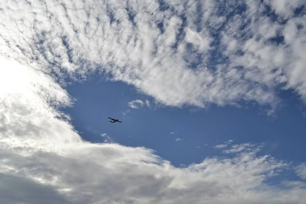 Tiefflug eines Flugzeugs in den blauen wolkenverhangenen Himmel — Stockfoto