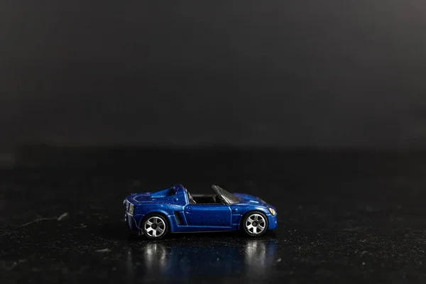 Foto selectivo de un coche deportivo de juguete azul en una superficie negra — Foto de Stock