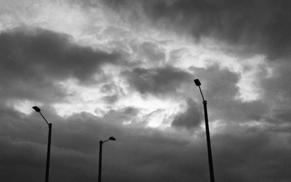 Low angle grey scale shot of lamp posts under the beautiful cloudy sky — Stock fotografie