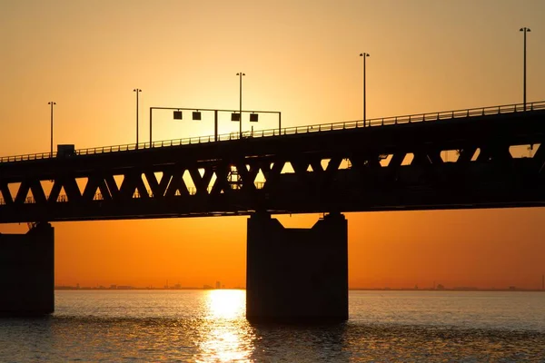 Silhouet van een brug over de zee met de zon op de achtergrond — Stockfoto