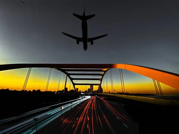 Letadlo nad mostem s pohybovým světelným efektem během západu slunce večer — Stock fotografie
