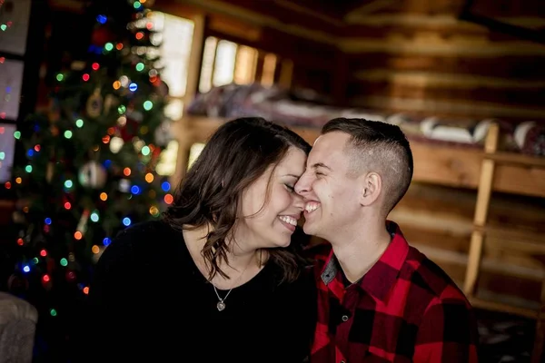 Happy couple sitting in a wooden cottage near the Christmas tree — Foto de Stock