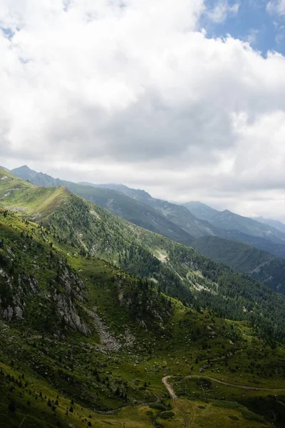 Paesaggio di colline ricoperte di verde con montagne rocciose sotto un cielo nuvoloso sullo sfondo — Foto Stock