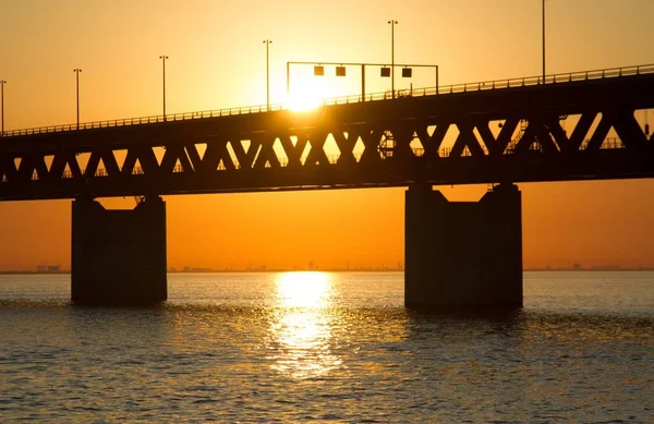 뒤에 주황 하늘이 보이는 물 위를 가로지르는 위치 ktspunkt öresundsbron 다리의 실루엣 — 스톡 사진