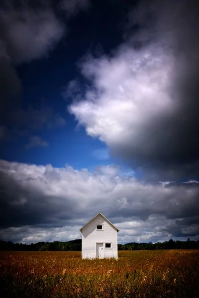 Vue verticale d'une cabane blanche dans un champ herbeux sous les nuages de tempête — Photo