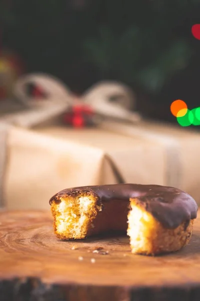 Vertical closeup of half bitten chocolate-dipped doughnut with a blurry festive background — Stock Photo, Image