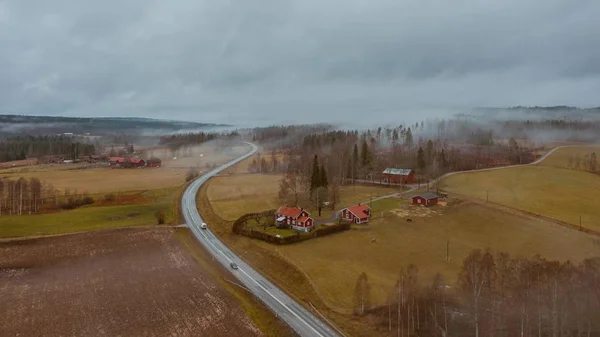 High angle shot of a road surrounded by a field with a frozen lake in the middle in Sweden — ストック写真