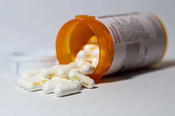 stock image A closeup shot of white capsules pouring out of the bottle on a white surface