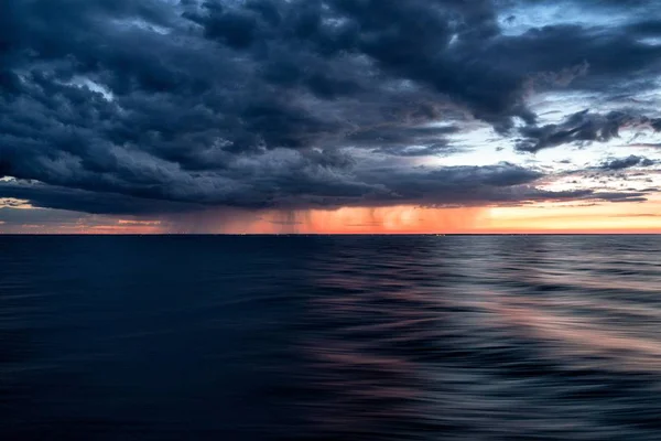 Nuvens escuras do céu do por do sol sobre a água escura do oceano — Fotografia de Stock