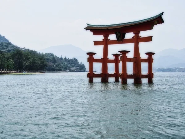 Santuario Itsukushima en un mar con colinas cubiertas de bosques con un fondo borroso en Japón — Foto de Stock