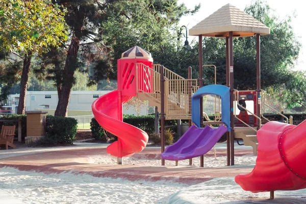 Барвисті слайди на дитячому майданчику в парку з деревами на задньому плані — стокове фото