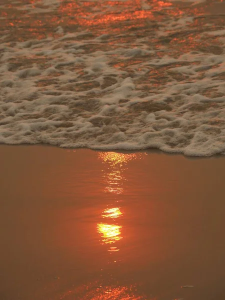 Praia cercada pelo mar durante um pôr do sol à noite com o sol refletindo sobre a água — Fotografia de Stock