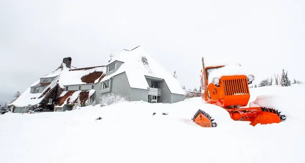 Orange tractor in front of a house buried in snow — Stock Photo, Image