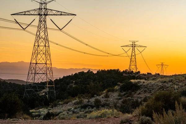 View of high power electricity poles on green hills during sunset time — Stock Photo, Image