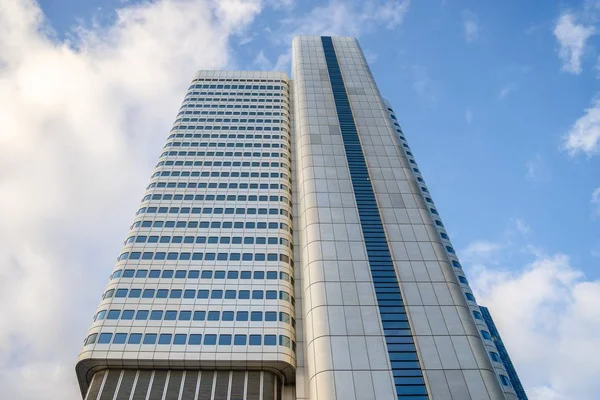 Vista de ângulo baixo de um edifício alto com janelas azuis sob um céu nublado e luz solar — Fotografia de Stock
