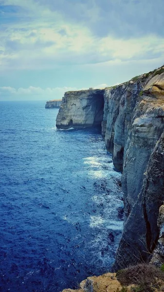 Vertical shot of a rock formation at the ocean shore under the cloudy sky — 스톡 사진