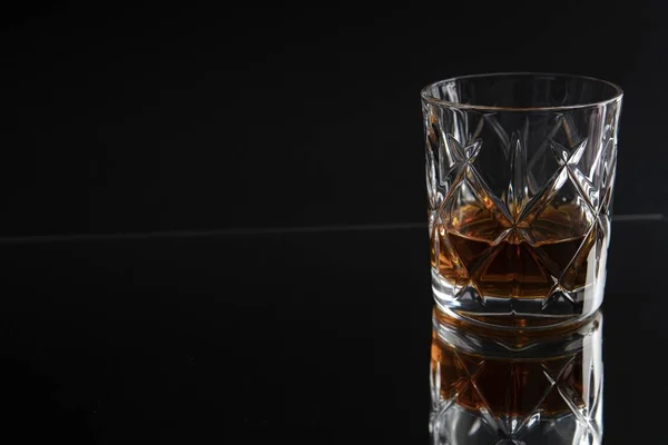 Sticlă de whisky reflectând pe o masă pe un fundal negru — Fotografie, imagine de stoc